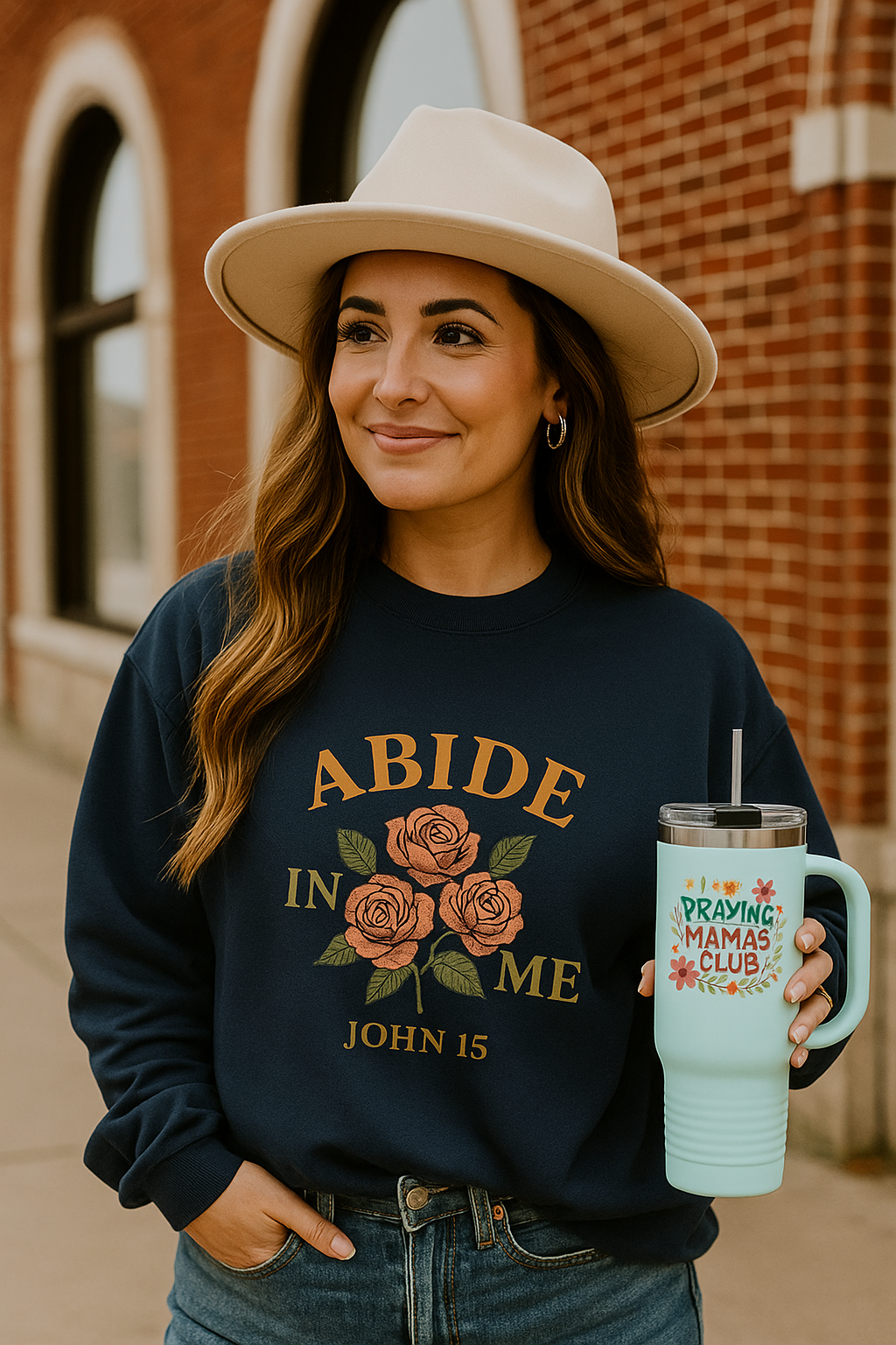 Woman wearing a navy “Abide in Me – John 15” Christian sweatshirt with rose design, smiling outside a brick building. Faith-based apparel from The Bougie Pumpkin Boutique.